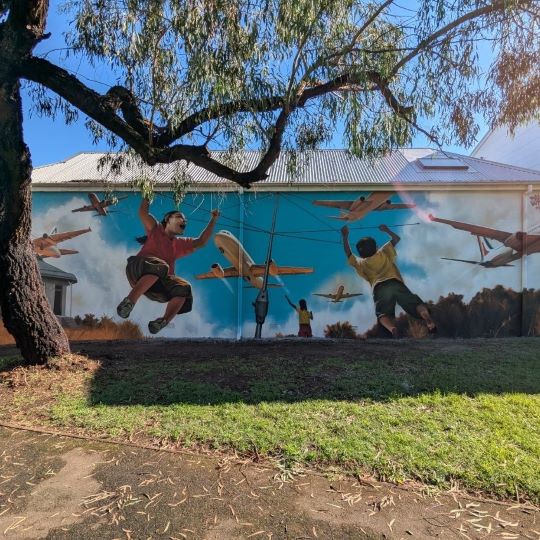 A mural painting of a girl swinging on a hills hoist while an aeroplane flies overhead.